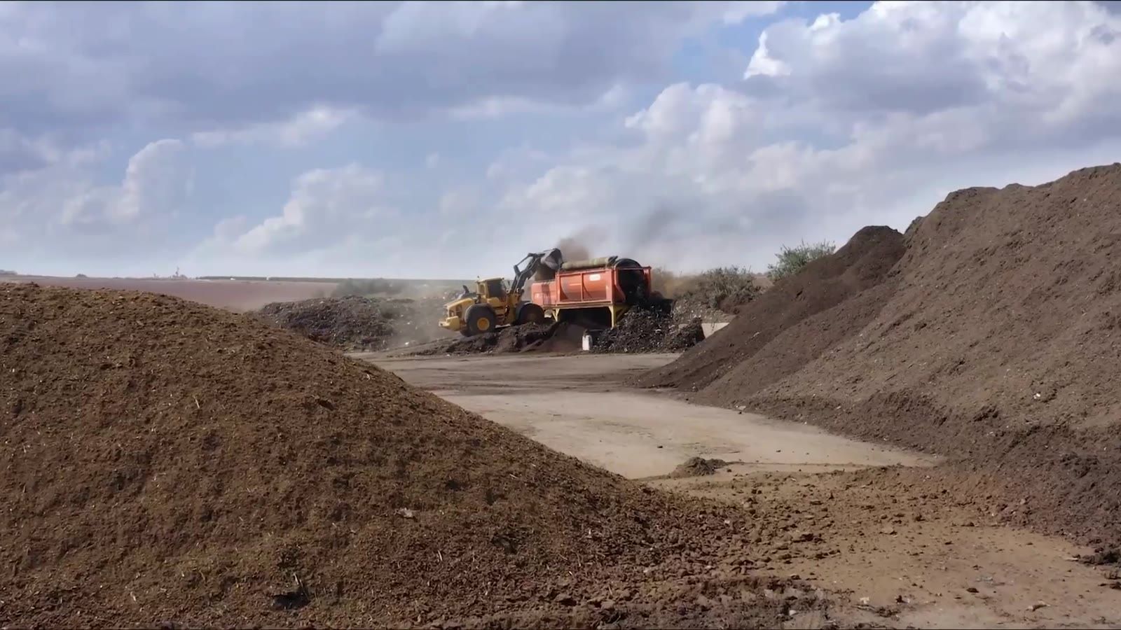Soil and compost heaps at a processing site, with a loader at work