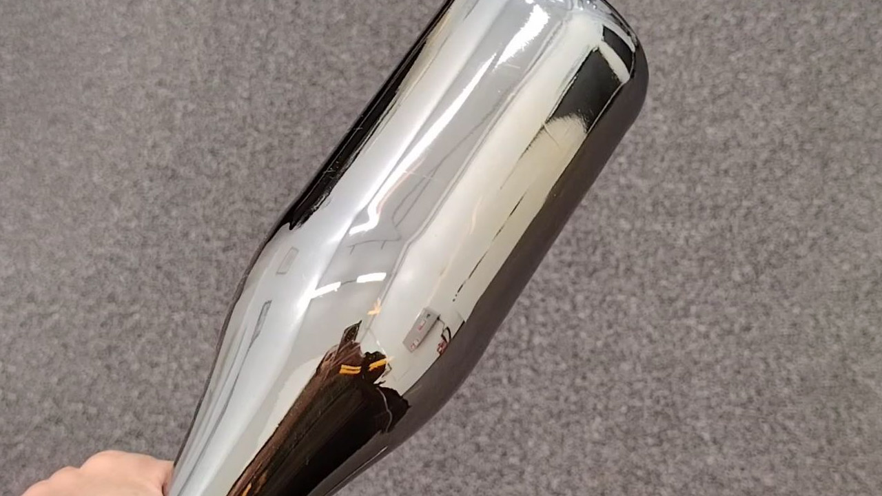 A hand holding a bottle with a mirror-metallic coating